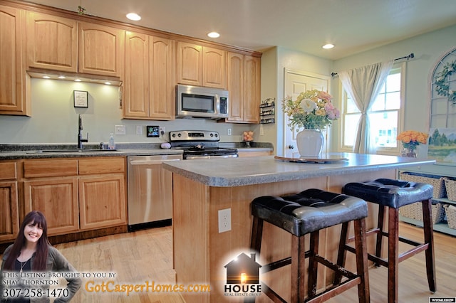 kitchen with light wood-type flooring, a sink, a kitchen island, stainless steel appliances, and a breakfast bar area