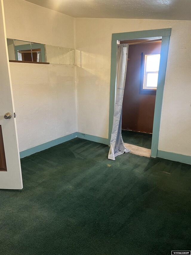 unfurnished room featuring baseboards and dark carpet