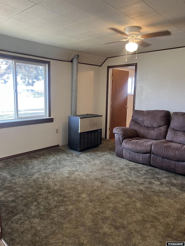 unfurnished living room with plenty of natural light, carpet, ceiling fan, and a wood stove