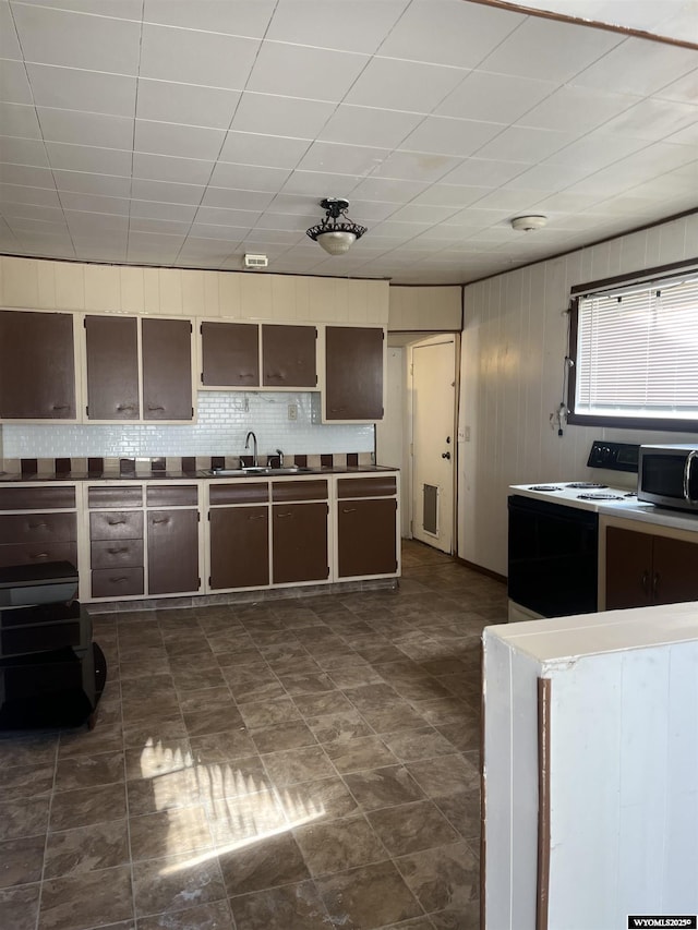 kitchen featuring white range with electric stovetop, tasteful backsplash, wood walls, stainless steel microwave, and a sink