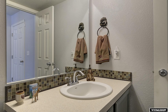 bathroom featuring backsplash, a textured wall, and vanity