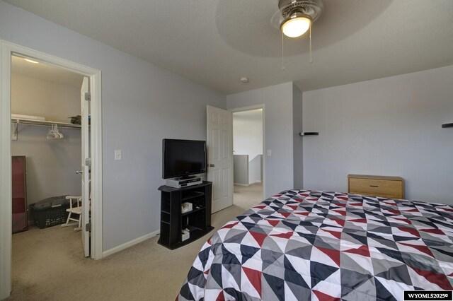 bedroom featuring light carpet, a walk in closet, a closet, baseboards, and ceiling fan