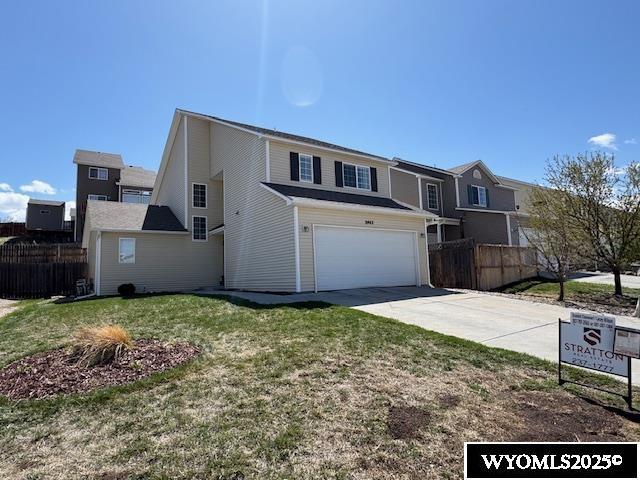 traditional-style home featuring a front yard, an attached garage, concrete driveway, and fence