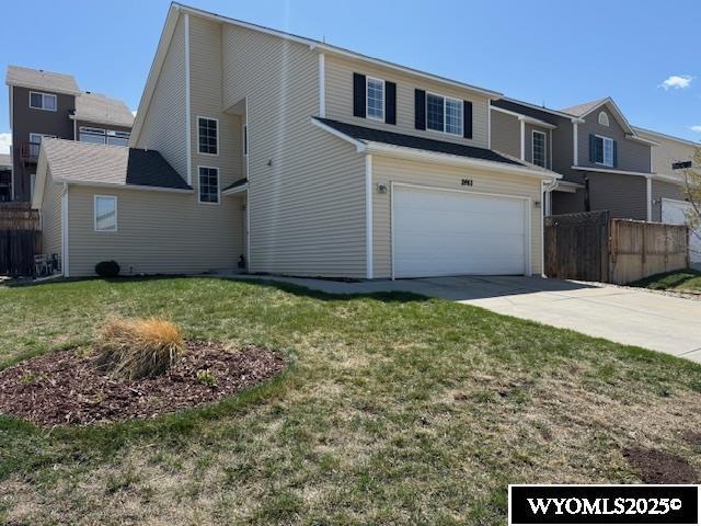 traditional-style home with an attached garage, a front yard, concrete driveway, and fence