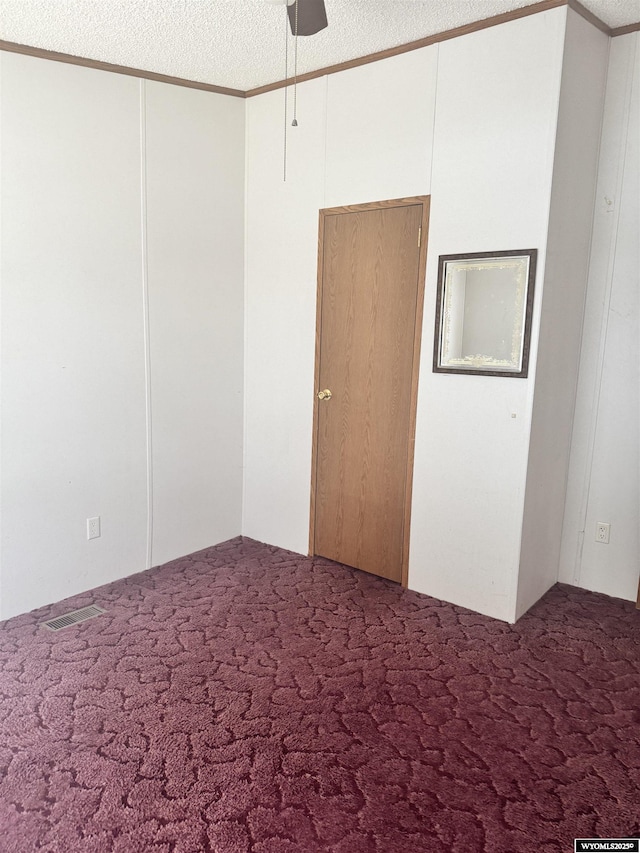 carpeted spare room with a ceiling fan, ornamental molding, a textured ceiling, and visible vents