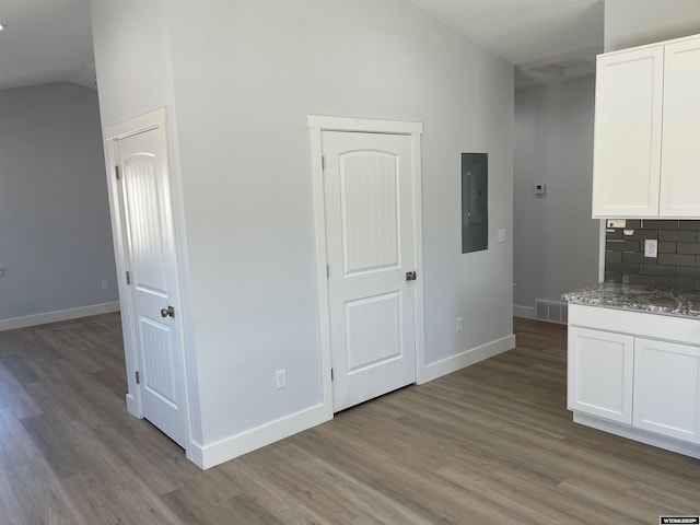 kitchen with lofted ceiling, electric panel, and light wood finished floors