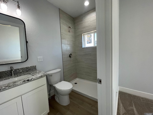 bathroom with a tile shower, baseboards, toilet, and vanity