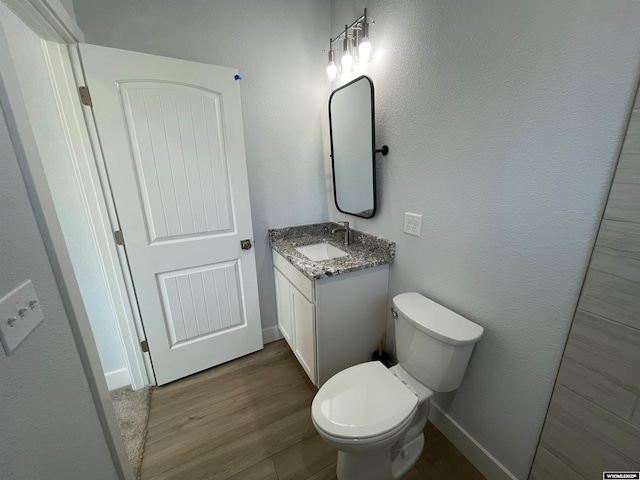 bathroom with baseboards, wood finished floors, vanity, and toilet