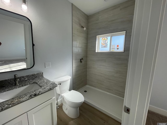 bathroom featuring a tile shower, vanity, toilet, and baseboards