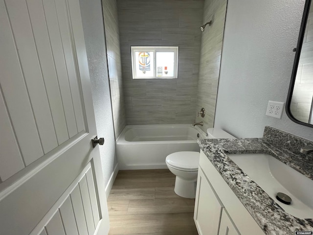 bathroom featuring a textured wall, wood finished floors, shower / bath combination, toilet, and vanity