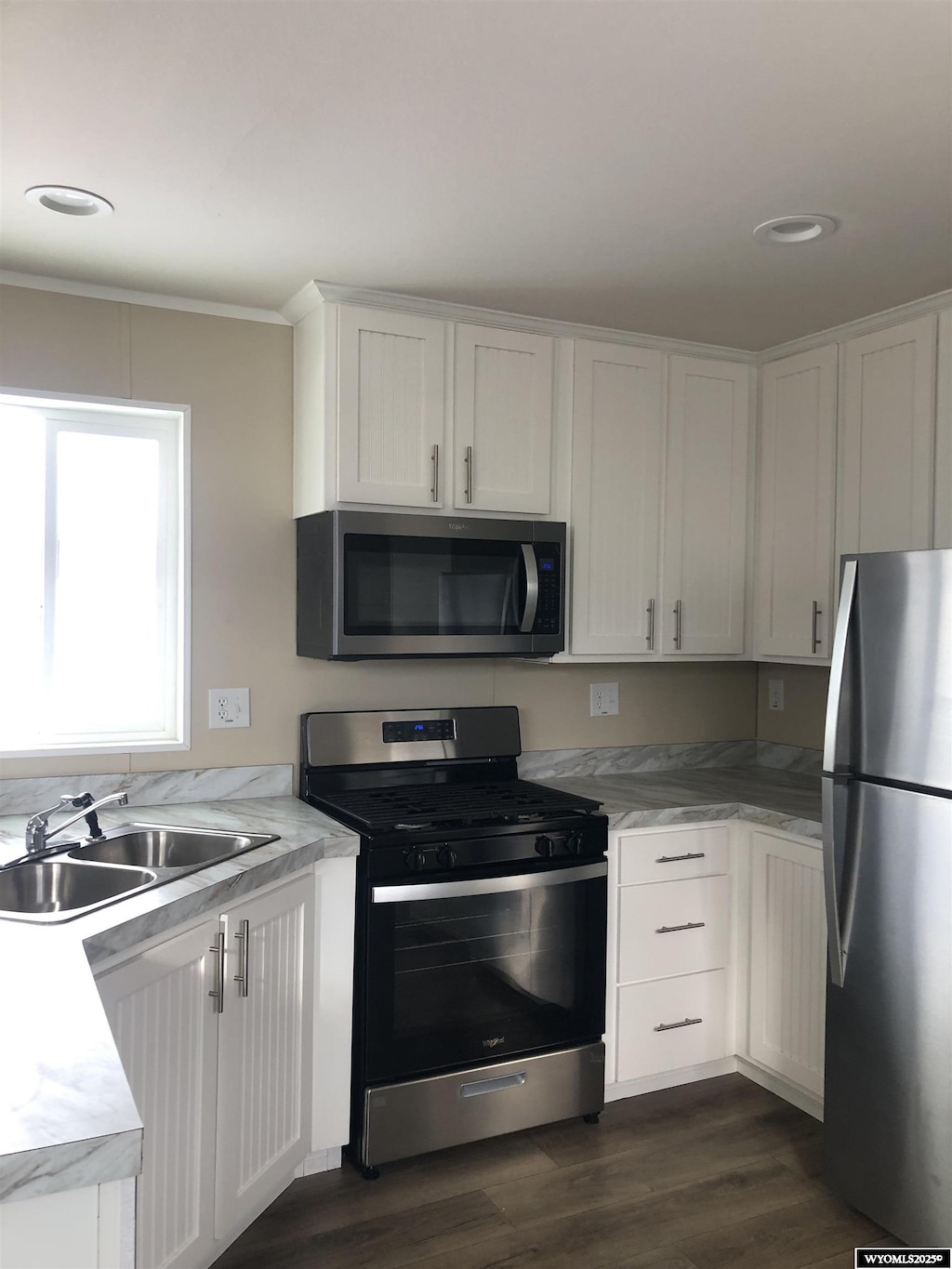 kitchen with light countertops, stainless steel appliances, dark wood finished floors, white cabinetry, and a sink