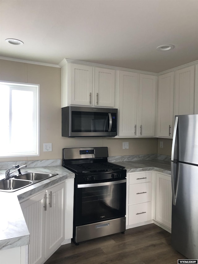 kitchen with light countertops, stainless steel appliances, dark wood finished floors, white cabinetry, and a sink