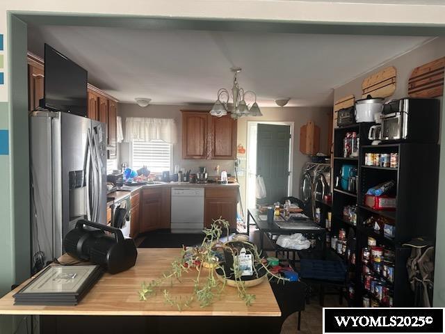 kitchen featuring washing machine and dryer, light countertops, stainless steel fridge with ice dispenser, dishwasher, and an inviting chandelier