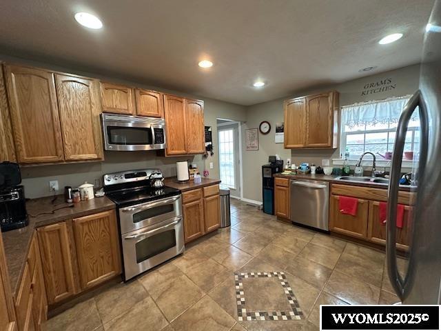 kitchen with light tile patterned flooring, dark countertops, recessed lighting, appliances with stainless steel finishes, and a sink