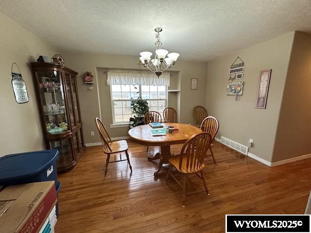 dining room with wood finished floors, a notable chandelier, baseboards, and visible vents