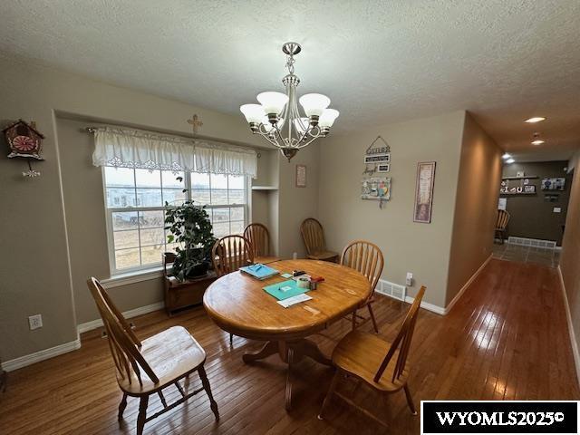 dining space featuring a textured ceiling, wood-type flooring, visible vents, and a chandelier