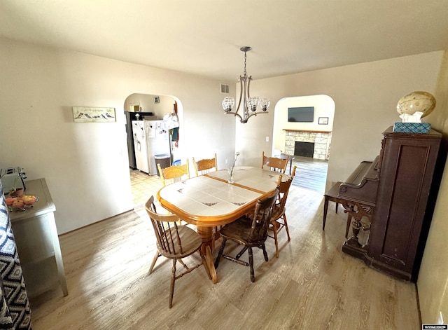 2842 Main St, Torrington, WY 82240 - dining space with light wood-type flooring, arched walkways, a fireplace, and an inviting chandelier