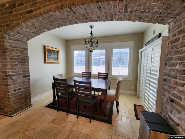 303 Tamarack Dr, Rock Springs, WY 82901 - dining room with an inviting chandelier, brick wall, stone tile floors, and baseboards