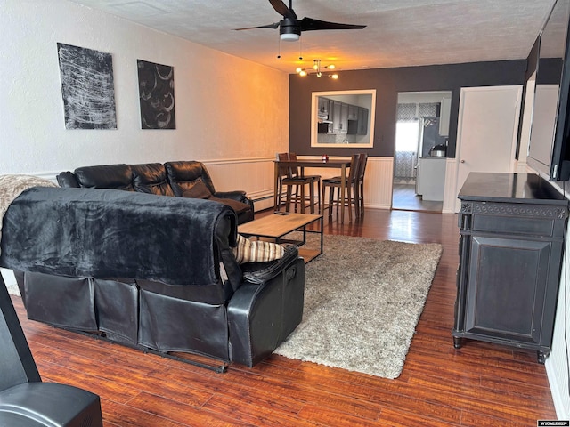 living area with a textured ceiling, a textured wall, dark wood-type flooring, and a ceiling fan