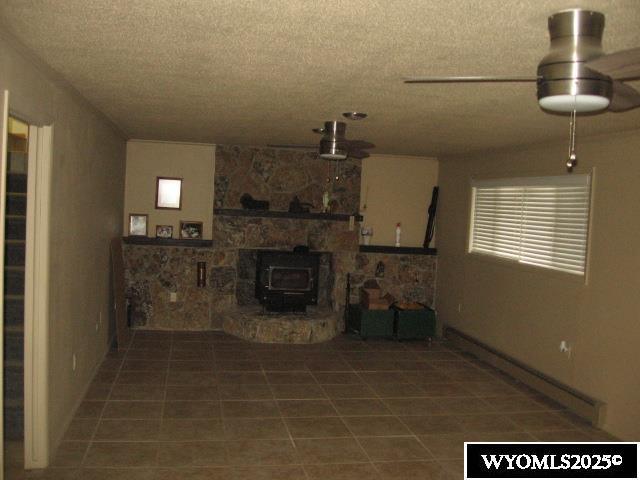 unfurnished living room featuring tile patterned floors, a wood stove, a baseboard heating unit, and a textured ceiling