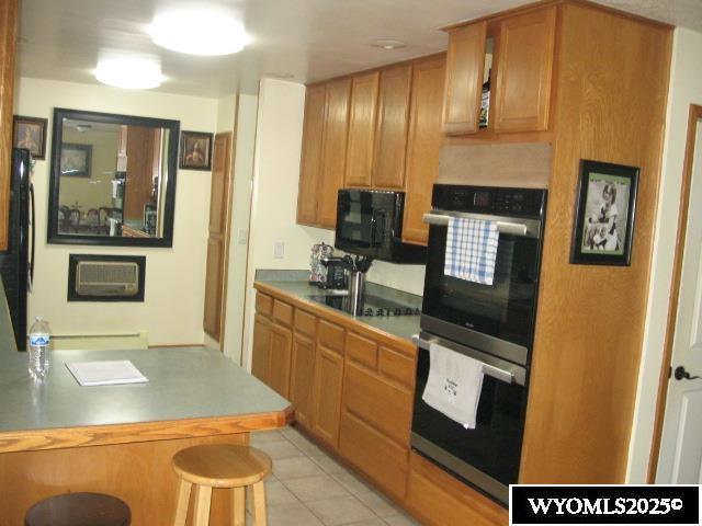 kitchen featuring a wall unit AC, light tile patterned floors, a breakfast bar, black appliances, and baseboard heating