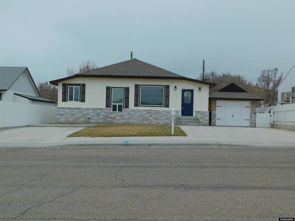 view of front of property featuring an outdoor structure, cooling unit, concrete driveway, fence, and stone siding