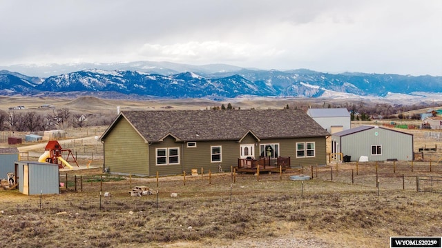 back of house with a deck with mountain view, an outdoor structure, fence, and a playground