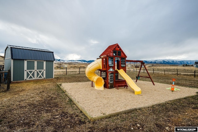 view of playground featuring fence, a shed, an outdoor structure, and a mountain view