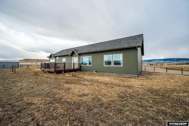 back of house with a deck with mountain view, a rural view, and roof with shingles