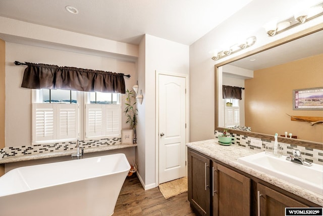 full bathroom with wood finished floors, tasteful backsplash, vanity, and a freestanding bath