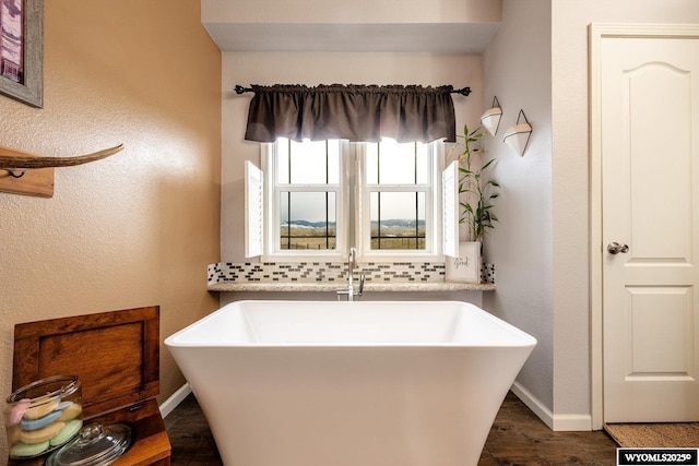 full bath with baseboards, decorative backsplash, a sink, and a freestanding tub