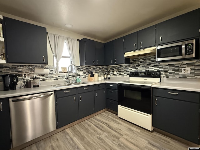 kitchen with light countertops, light wood-type flooring, stainless steel appliances, under cabinet range hood, and a sink