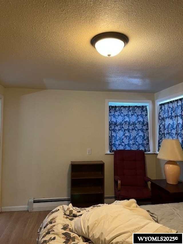 419 6th St, Rawlins, WY 82301 - bedroom with baseboards, a textured ceiling, wood finished floors, and a baseboard radiator