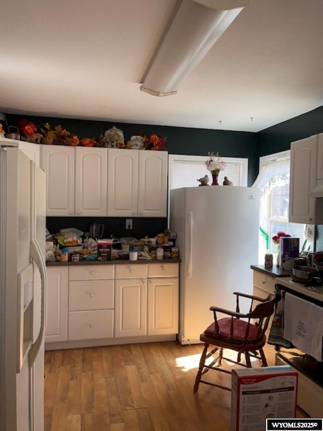 419 6th St, Rawlins, WY 82301 - kitchen featuring white refrigerator with ice dispenser, dark countertops, light wood finished floors, freestanding refrigerator, and white cabinets
