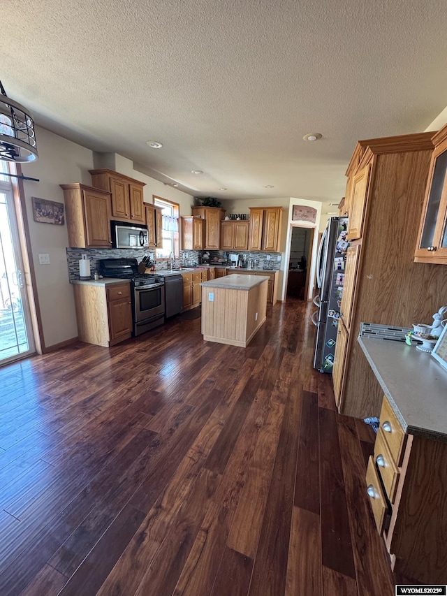 2720 State Highway 414 N, Lyman, WY 82937 - kitchen featuring brown cabinets, appliances with stainless steel finishes, a center island, decorative backsplash, and dark wood-type flooring