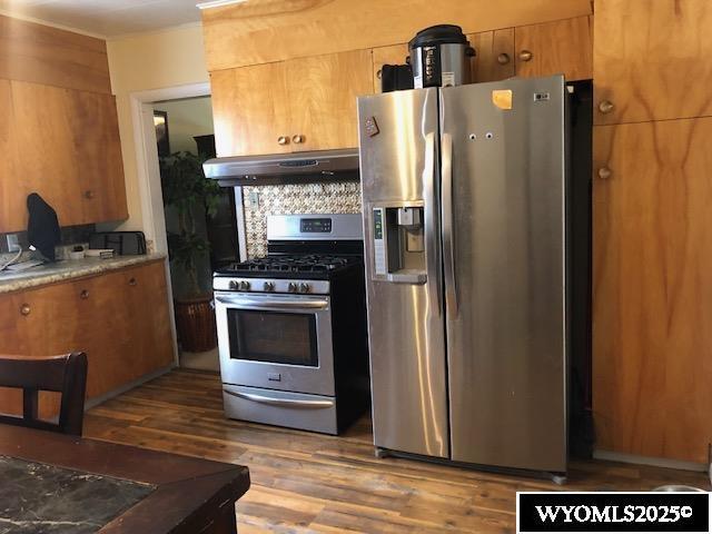 816 Center St, Rock Springs, WY 82901 - kitchen with brown cabinetry, appliances with stainless steel finishes, wood finished floors, under cabinet range hood, and backsplash