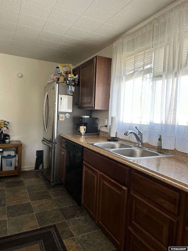 kitchen featuring stone finish floor, freestanding refrigerator, a sink, and black dishwasher
