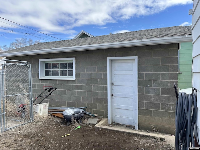 exterior space with roof with shingles, concrete block siding, and fence
