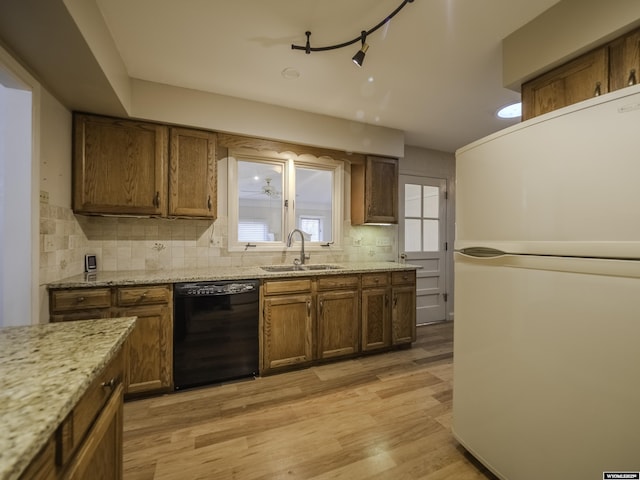 kitchen featuring tasteful backsplash, freestanding refrigerator, light wood finished floors, dishwasher, and a sink