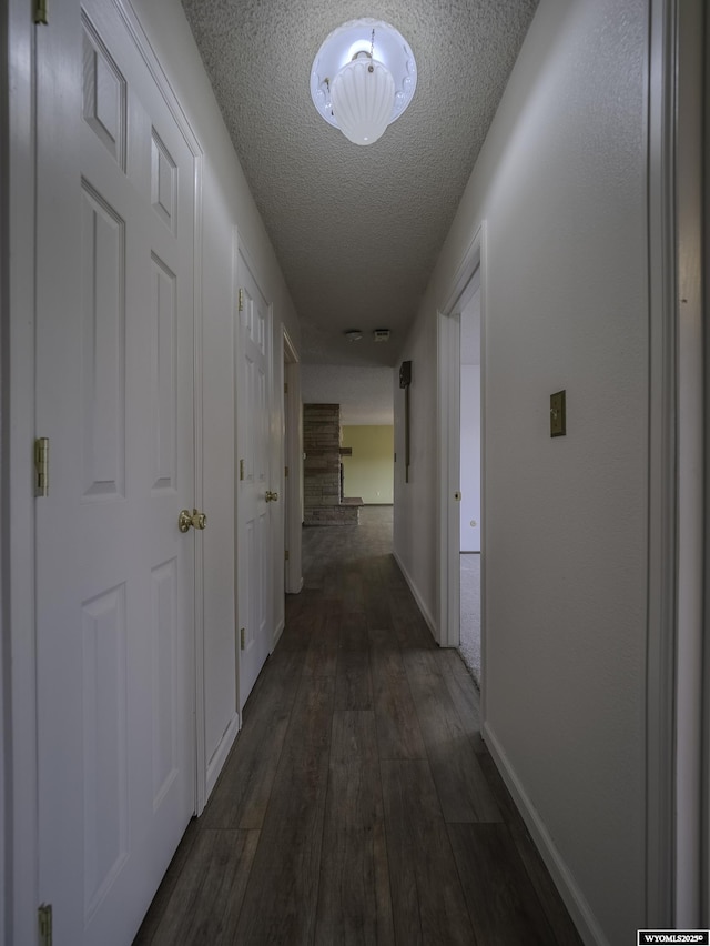 hallway with dark wood-style flooring, baseboards, and a textured ceiling