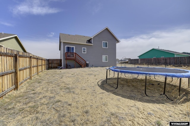back of property with a trampoline, a fenced backyard, and stairway