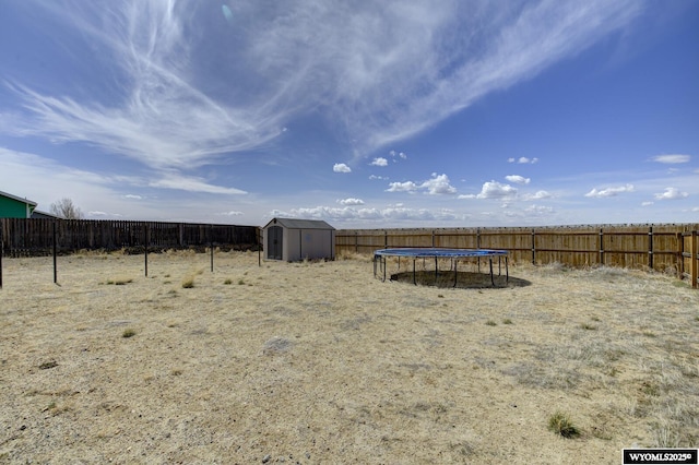 view of yard with a trampoline, an outdoor structure, a fenced backyard, and a shed