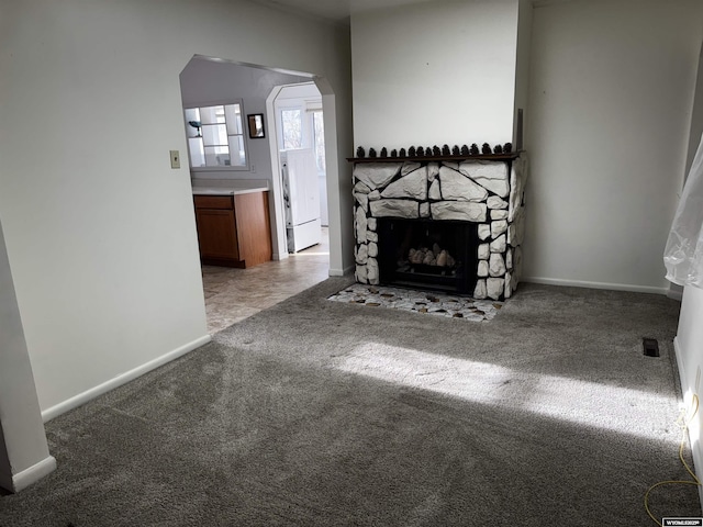 unfurnished living room featuring carpet flooring, arched walkways, baseboards, and a fireplace