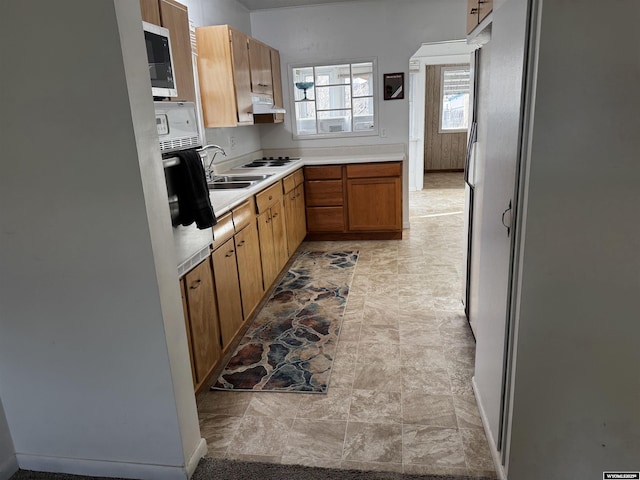 kitchen featuring stone finish floor, light countertops, stainless steel microwave, under cabinet range hood, and oven