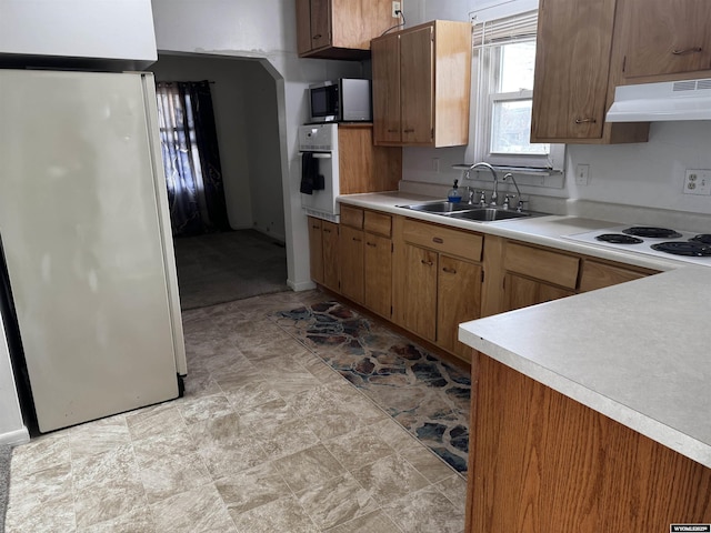kitchen with light countertops, under cabinet range hood, brown cabinets, a sink, and stainless steel appliances