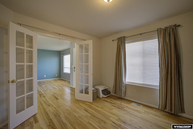 empty room featuring french doors, baseboards, visible vents, and wood finished floors