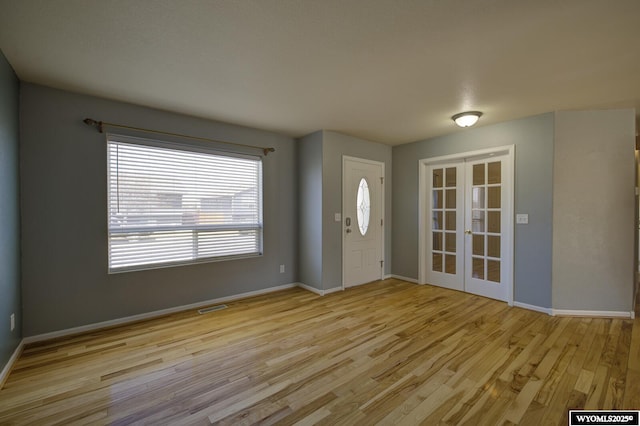 foyer featuring french doors, baseboards, light wood finished floors, and visible vents