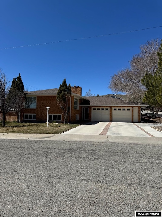 view of front facade with an attached garage, a chimney, concrete driveway, and brick siding