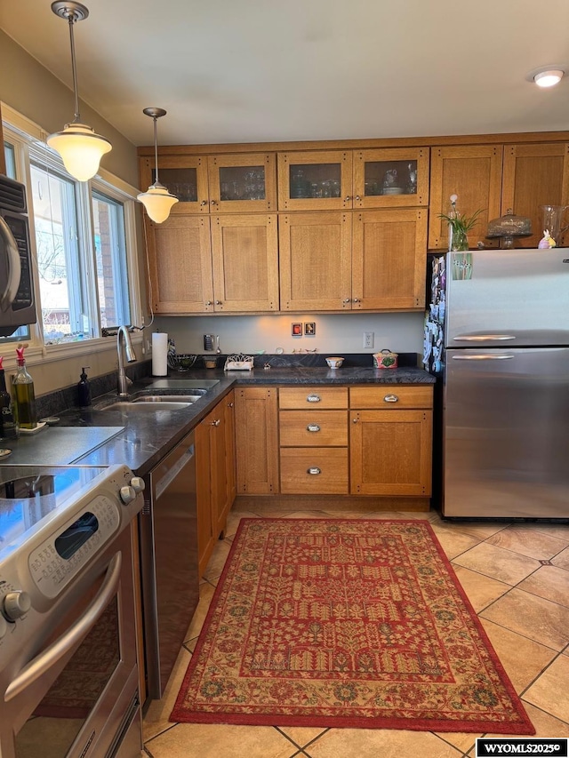 kitchen featuring dark countertops, brown cabinetry, appliances with stainless steel finishes, pendant lighting, and a sink