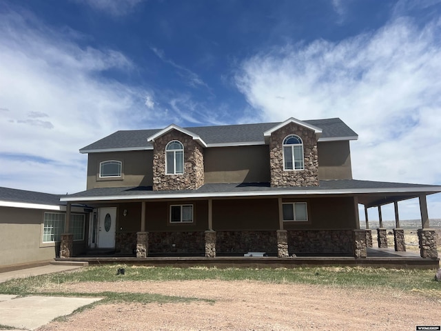 farmhouse inspired home with a porch, stucco siding, and stone siding